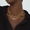 A close-up of a gold layered Cuban link necklace worn around the neck against a black top.