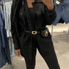 A person models a black PU leather belt bag with a gold metal buckle and matching pants.