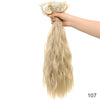 Una mano sostiene un mechón de extensiones de cabello rubio y ondulado, sujetas con un clip decorativo.