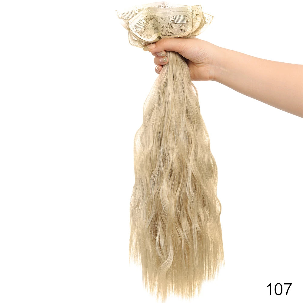 Una mano sostiene un mechón de extensiones de cabello rubio y ondulado, sujetas con un clip decorativo.