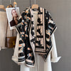 A black and beige plaid cashmere scarf and shawl wrap displayed on a hanger against a neutral gray background.
