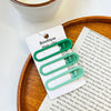 A white card displaying a set of vintage frosted green geometry hair clips on a wooden tray.