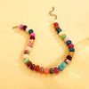 A necklace made of colorful resin beads in shades of pink, red, green, and white, strung on a gold chain.