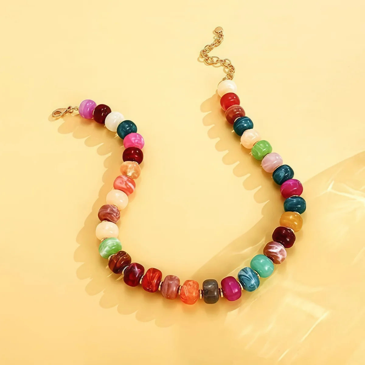 A necklace made of colorful resin beads in shades of pink, red, green, and white, strung on a gold chain.
