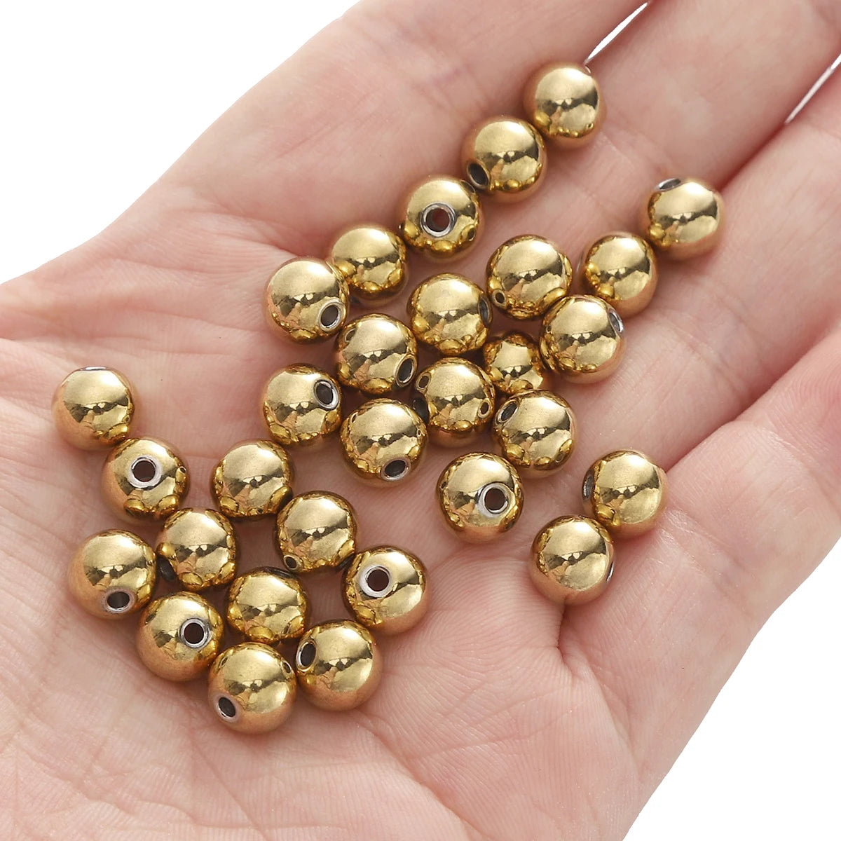A hand holds a cluster of small, round gold-colored stainless steel spacer beads for DIY jewelry making.