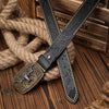 A black PU leather belt with a floral engraving and brass buckle is laid across a thick rope on a wooden surface.