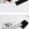 Gros plan d'un large ceinture élastique noire avec un accent texturé doré, présentée à côté d'un morceau de papier.