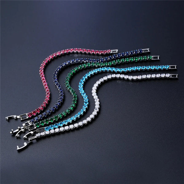A display of multiple iced out crystal tennis bracelets in various shades of pink, blue, green, and clear.