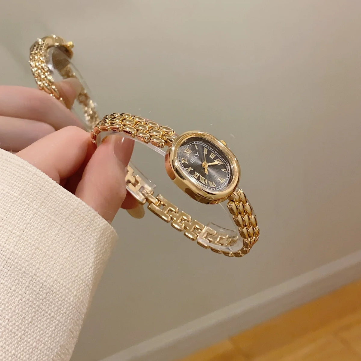 A hand is holding a gold-toned quartz fashion wristwatch with a mesh bracelet and clear crystal face.