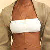 A close-up of a model wearing a gold adjustable belly chain body jewelry over a white crop top and beige jacket.