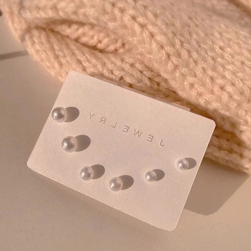 A small white card displaying three round stud earrings on a beige knitted fabric background.