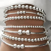 A set of silver minimalist round beaded bracelets worn on a person's wrist.