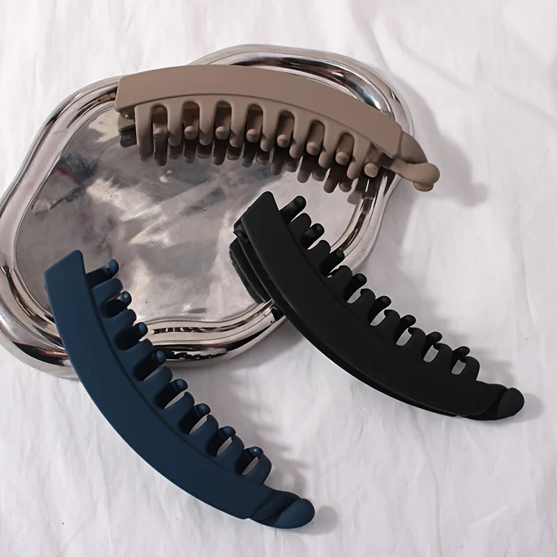 A set of large banana hair clips in beige and black are displayed on a white surface.
