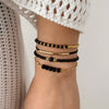 A close-up of a wrist wearing a stack of bohemian pearl beaded bracelets on a person's arm.