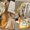 A floral print silk scarf in white and orange tones draped over a beige blazer.