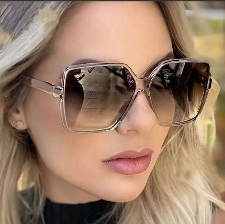 A close-up photo of a woman wearing oversized gradient sunglasses with light brown lenses and silver frames.