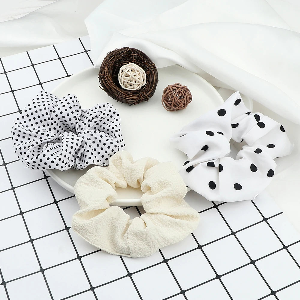 A flat lay showing three knitted hair scrunchie headbands in natural brown, white, and cream colors on a white surface.
