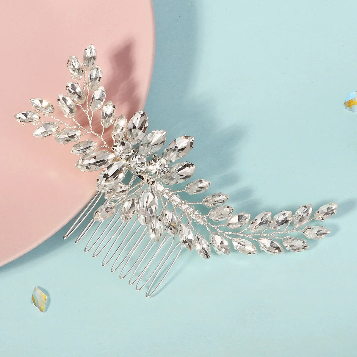 Une délicate peigne de cheveux pour mariée en cristal avec des feuilles scintillantes et de fins fils sur un fond bleu clair.
