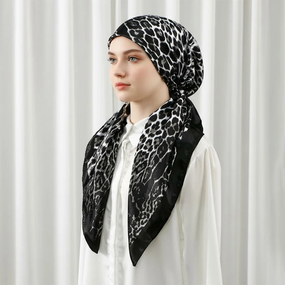 A woman wearing a black leopard print satin silk hijab headband cap with a white shirt.