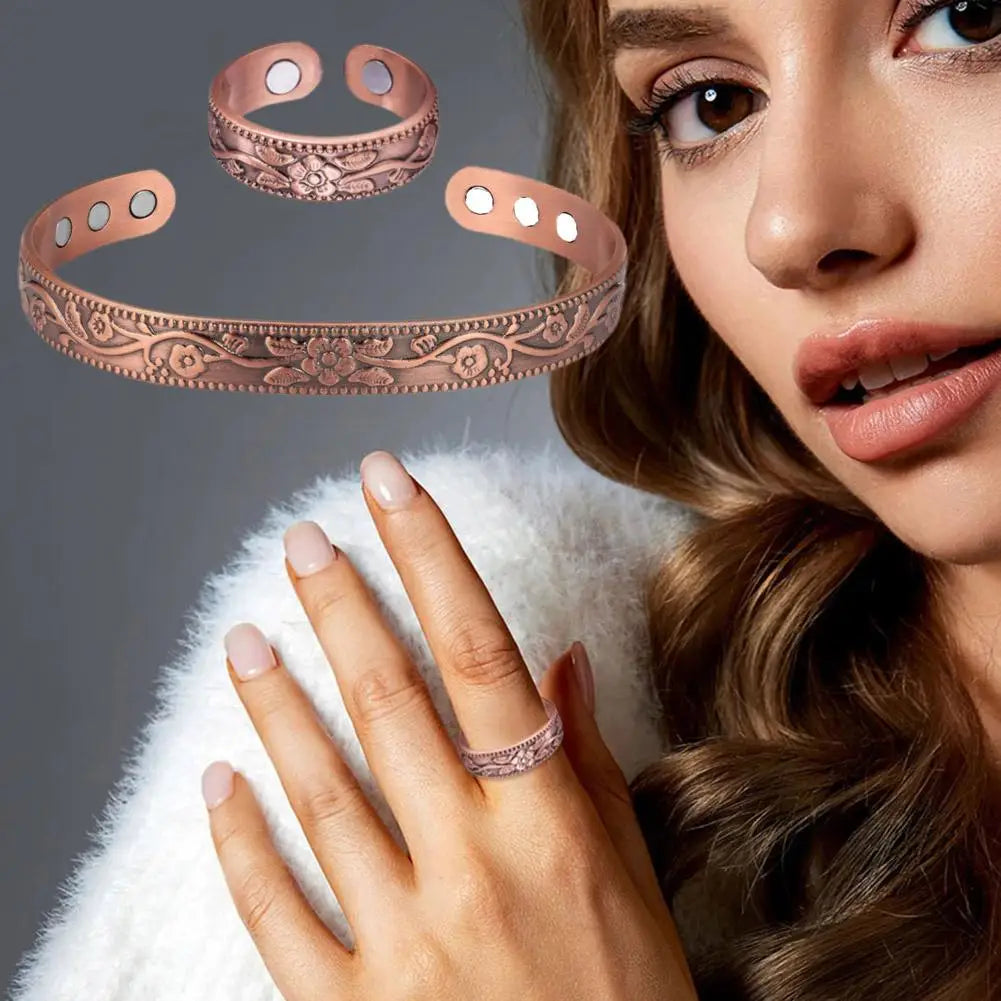 A close-up of a woman's hand wearing a vintage flower engraved copper bracelet and ring set.