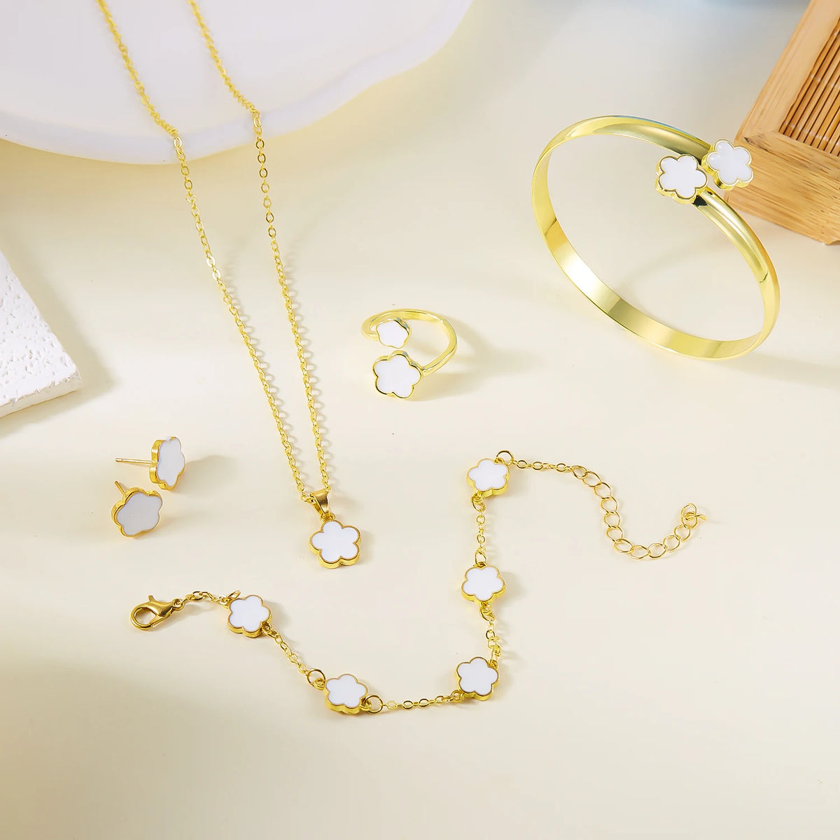 A set of five gold-colored bracelets featuring white enamel plum blossoms displayed on a light background.