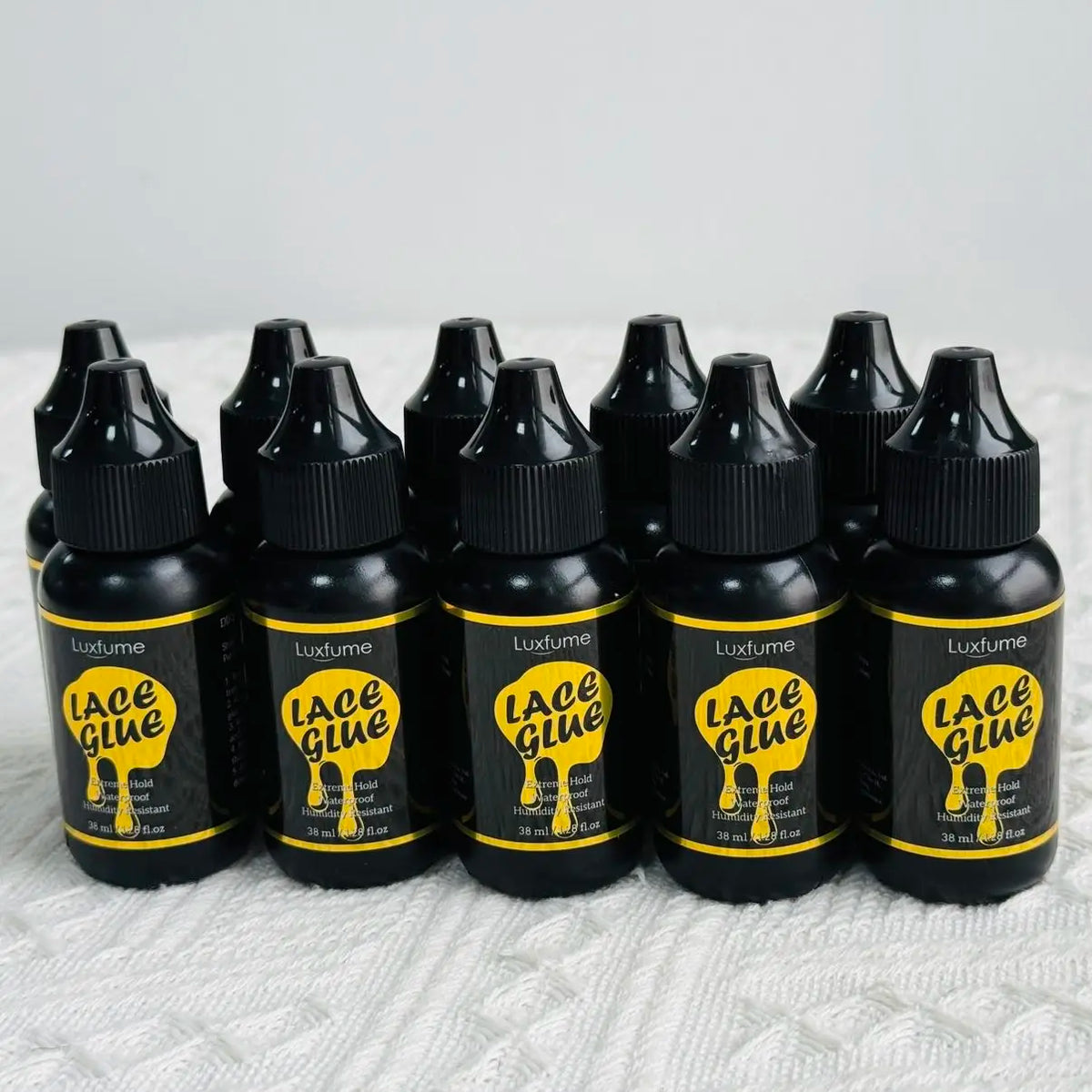 Eine Reihe schwarzer Glas-Pipettendr瓶e des Luxe Glue Produkts mit gelben Etiketten auf einer weißen Oberfläche.