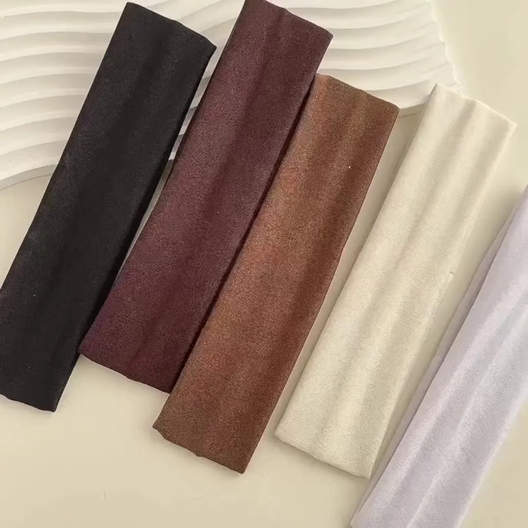 A collection of five solid colored fabric headbands for hair and fitness, including black, maroon, brown, beige, and light pu