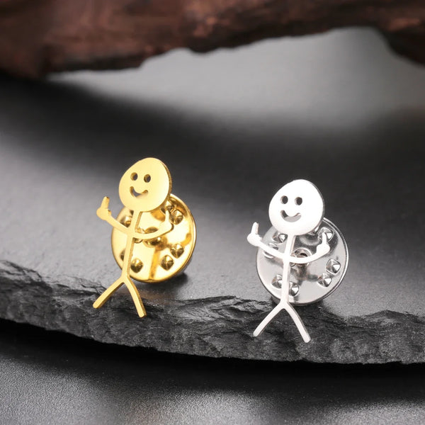 Gold and silver stickman brooches on a dark surface