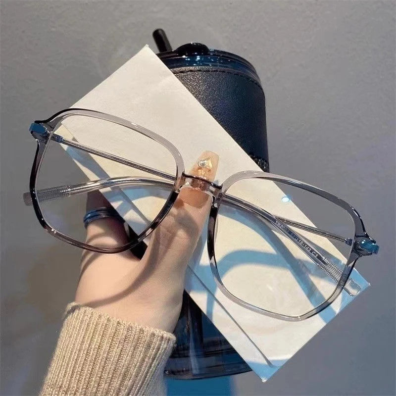 A pair of clear framed retro anti-blue light sunglasses resting on a white paper against a dark blue background.