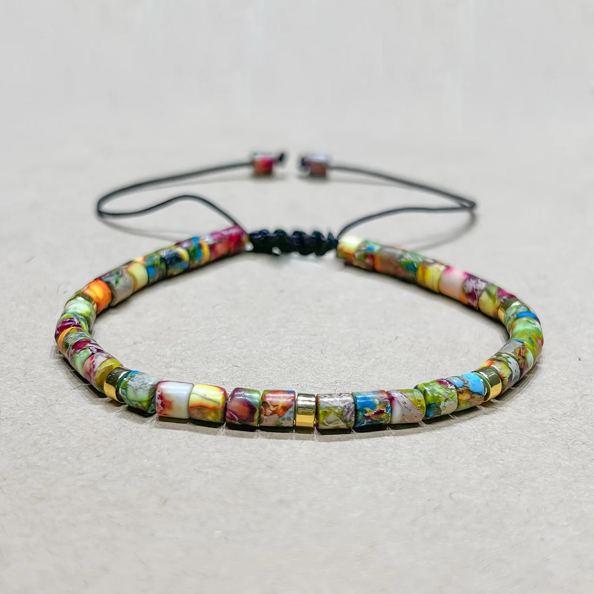 A friendship bracelet made of colorful natural stones and black cord, displayed on a light background.