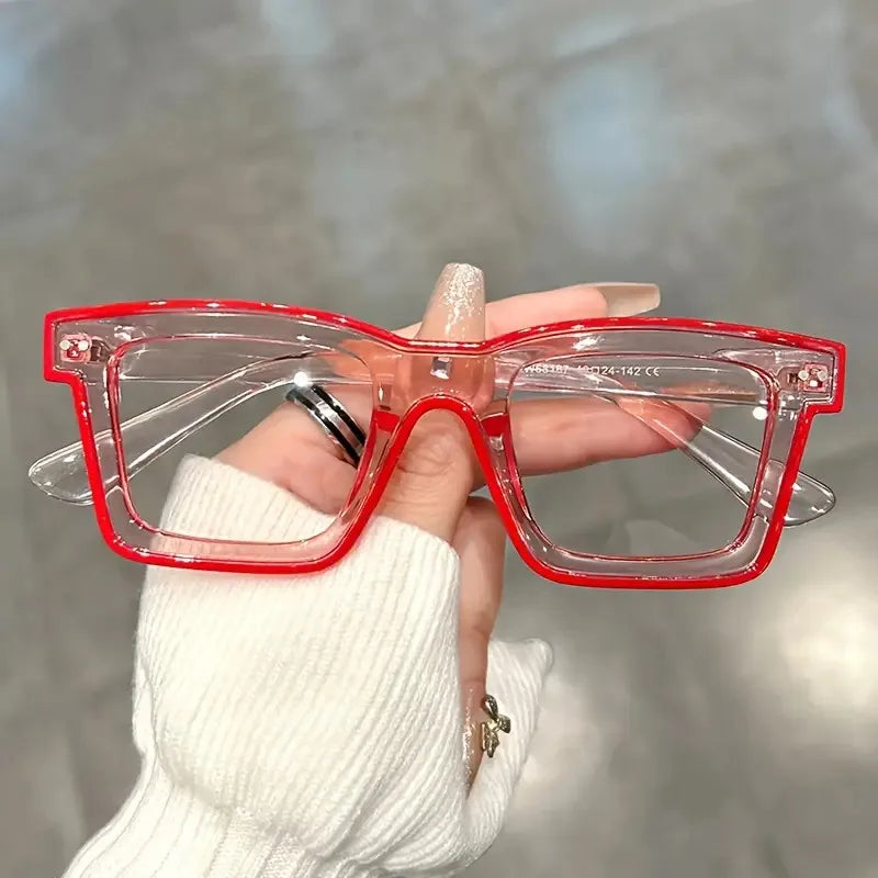 A hand holds a pair of red-framed costume glasses against a blurred gray background.