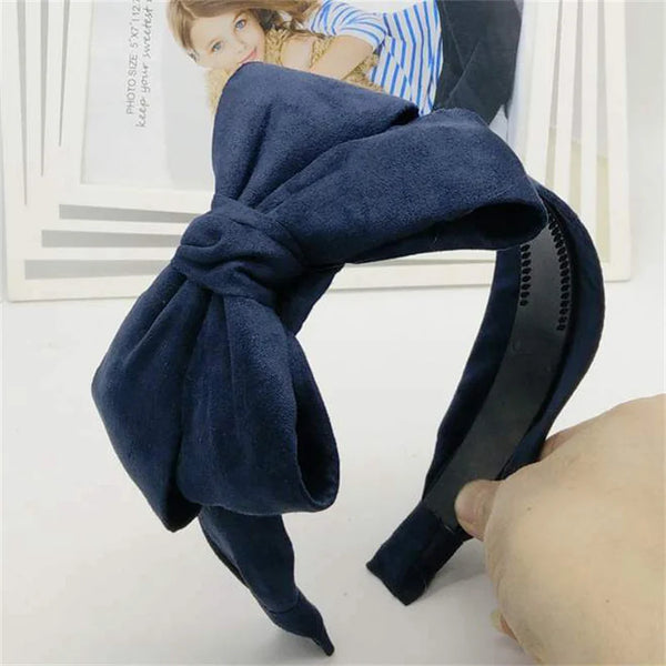 A dark navy blue velvet wide bow headband is shown being worn on a hand.