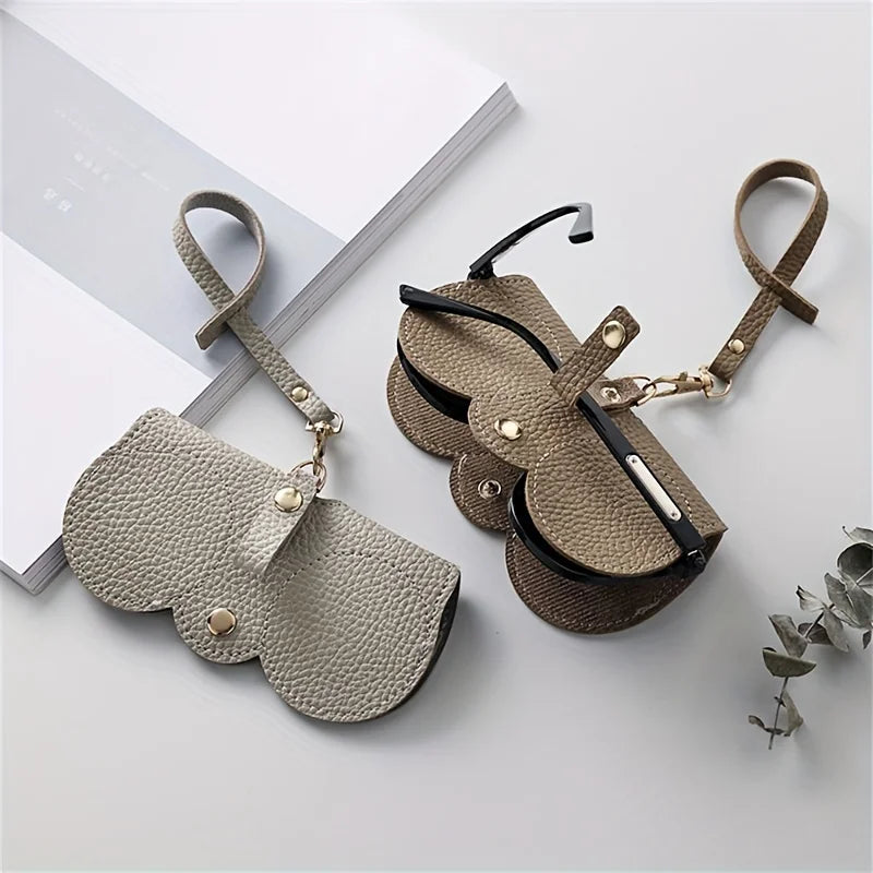 A beige PU leather pouch and glasses case with leather straps resting on a white surface.