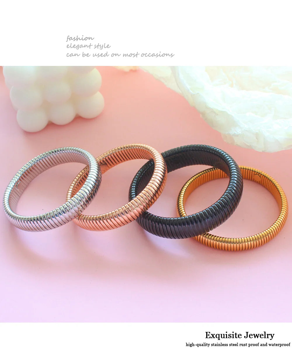 A collection of various gold-toned and silver stainless steel elastic bangle bracelets arranged on a pink surface.