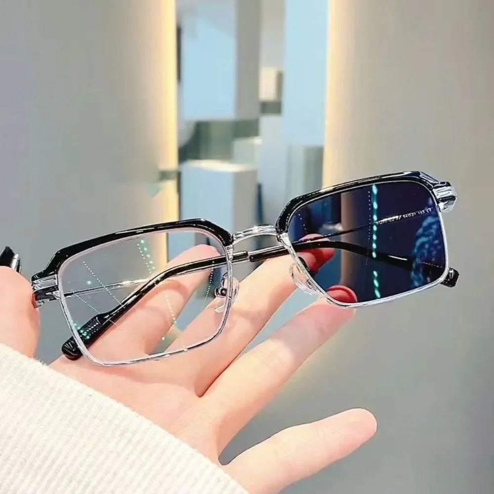 Une main tient une paire de lunettes de lecture photochromiques noires avec des verres anti-reflets bleus sur un fond clair.