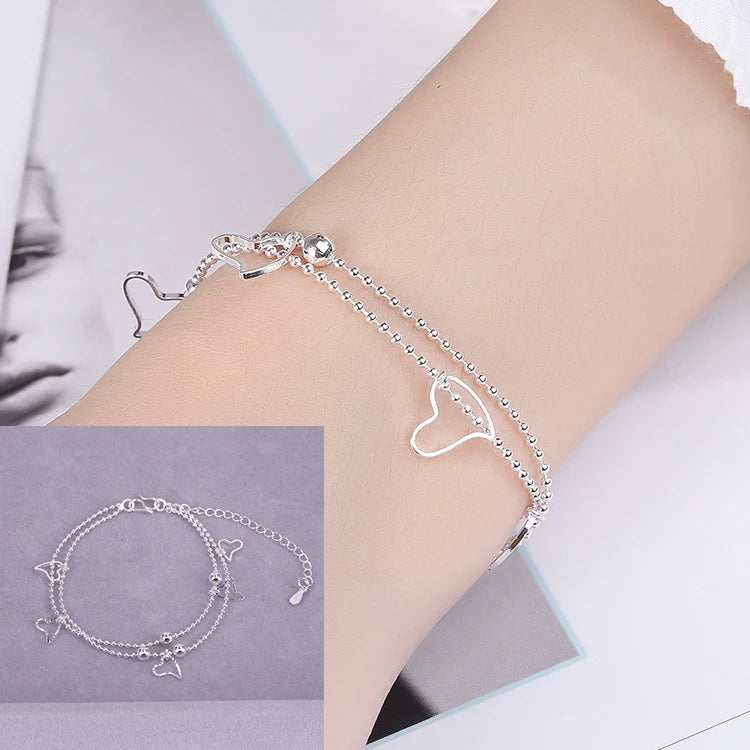 A close-up of a sterling silver double heart charm bracelet worn on a wrist.