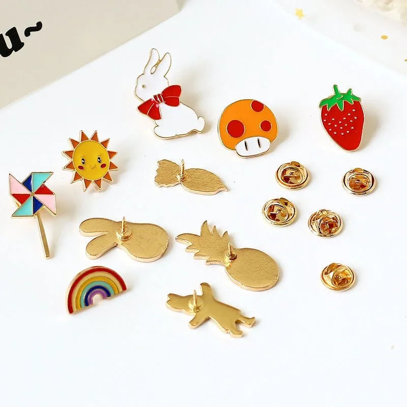 A collection of enamel badge pins featuring various designs including a bunny, strawberry, sun, rainbow, and gold-toned shape