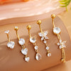 A set of five gold stainless steel dangled belly button rings with clear and floral charms displayed on a beige surface.