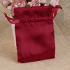 A deep red satin drawstring pouch filled with pink flowers, resting on a beige textured surface.