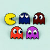 A set of four enamel pins shaped like Pac-Man characters in yellow, blue, red, and purple.
