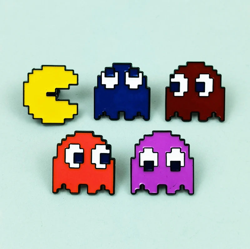 A set of four enamel pins shaped like Pac-Man characters in yellow, blue, red, and purple.