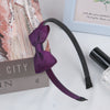 A purple grosgrain ribbon hair bow is displayed next to a book and a black cosmetic product.