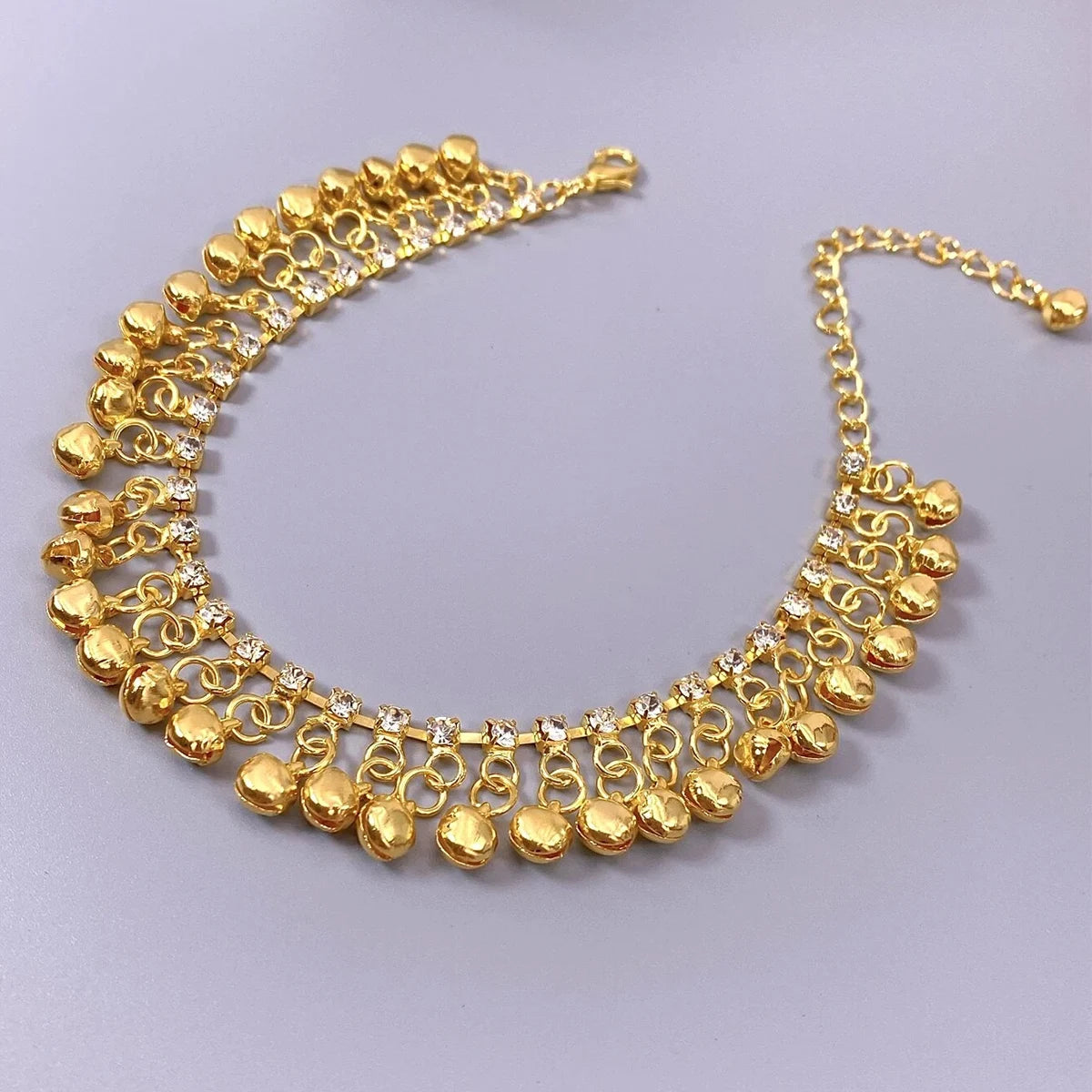 A gold bell foot chain anklet featuring small gold bells and clear stones.