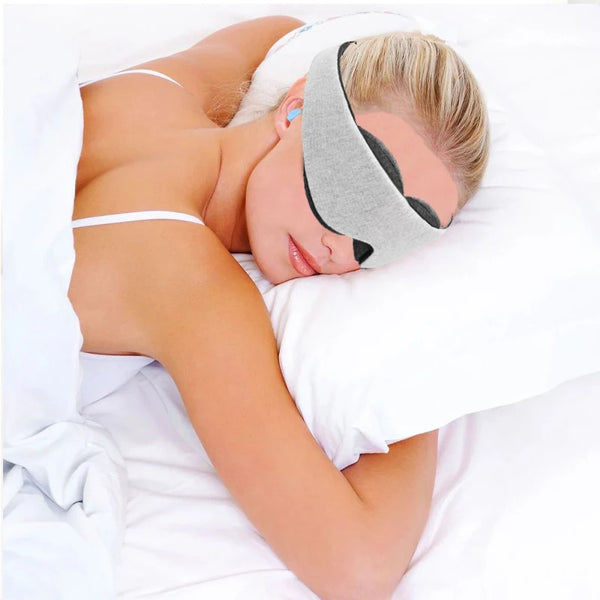 A person is wearing a gray 3D contoured sleep mask while lying down in bed.