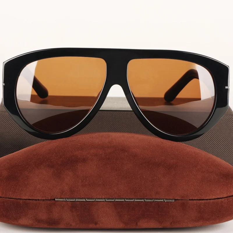 A pair of oversized pilot sunglasses with black frames and amber lenses resting on a brown velvet cushion.