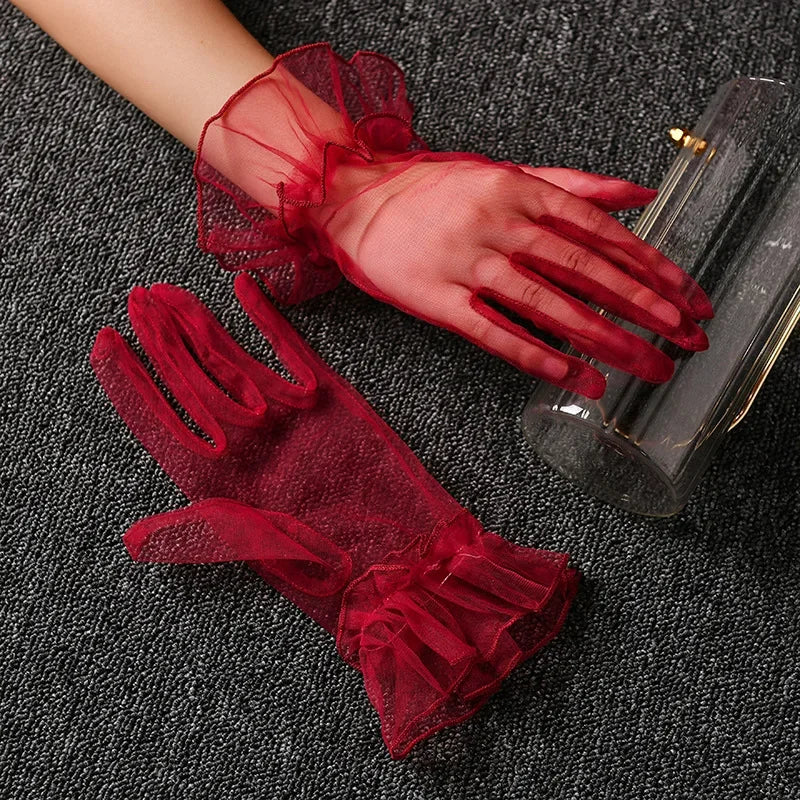 A pair of sheer red lace tulle finger gloves resting on a dark gray fabric.