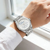 A close-up of a stainless steel watch with a blue dial and the slogan Who cares I'm already late on a person's wrist.