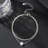 A delicate silver-plated chain anklet with a small flower charm displayed on a dark surface.