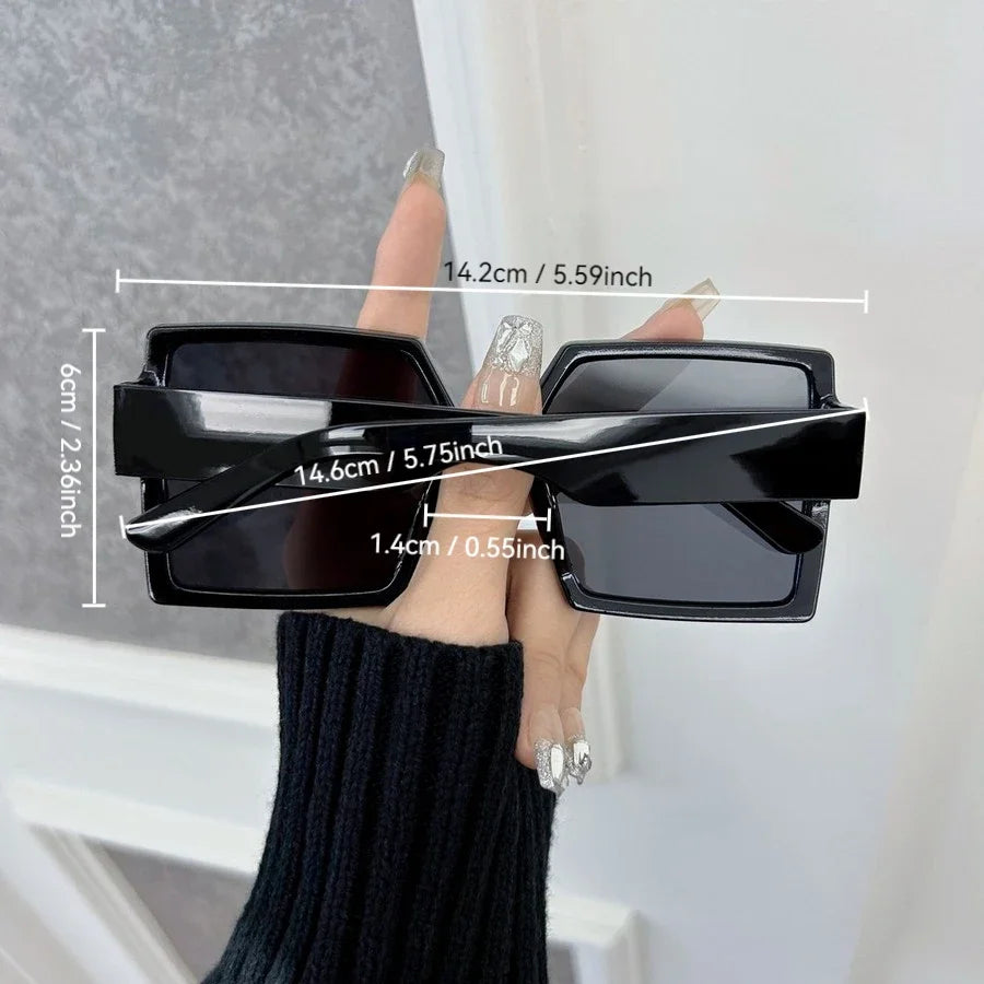 Black square mirror sunglasses being held by a hand, showing dimensions.