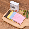 Un juego de cinco paños de limpieza de ante multicolor en varios tonos, dispuestos en una tabla de madera junto a una caja bl